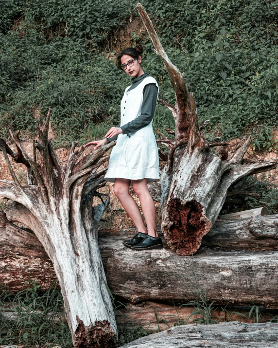 a woman wearing a white dress standing on top of a tree stump