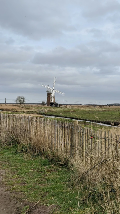 a windmill behind a wooden fence on a green grassy field