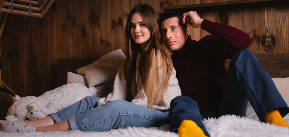 man and woman sitting on bed staring into the camera