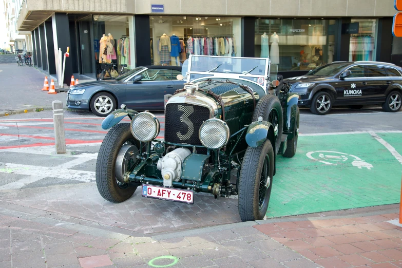 an old model car sits on the sidewalk beside a car