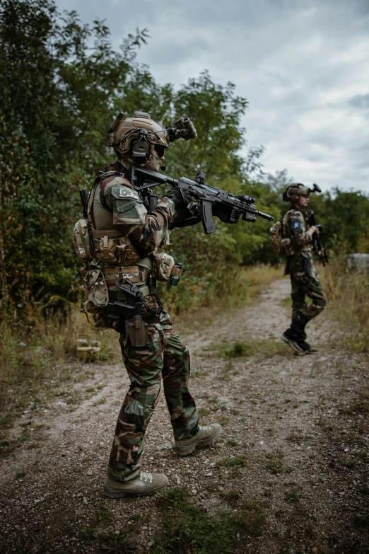 two soldiers in camouflage holding a gun and walking along a dirt path