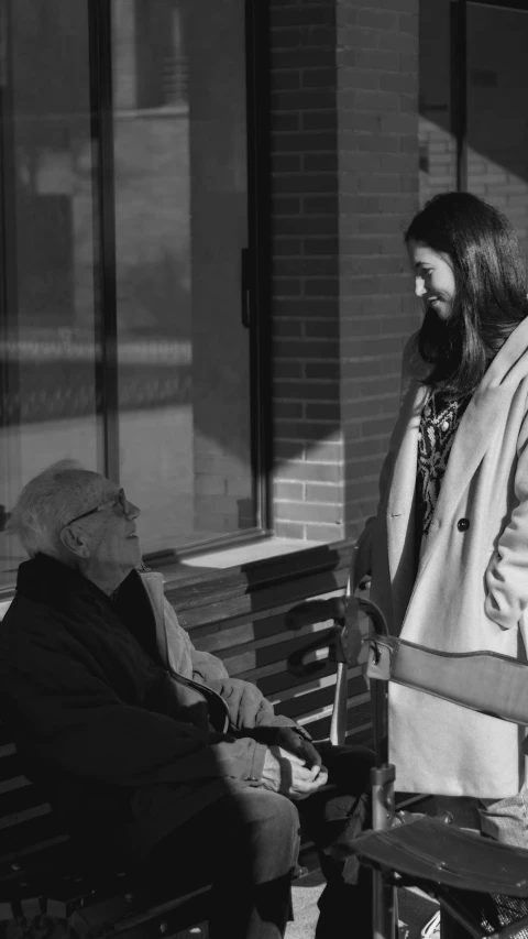 an old man in wheelchair talking to a young woman