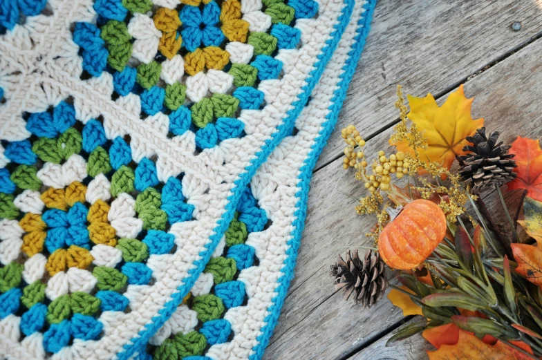 a crocheted blanket and an orange flower on a wooden table