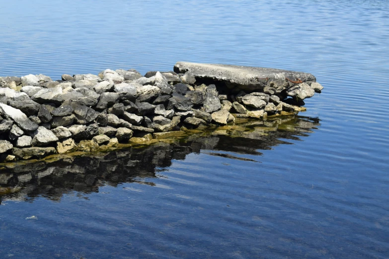 a bunch of rocks in water next to a rock wall