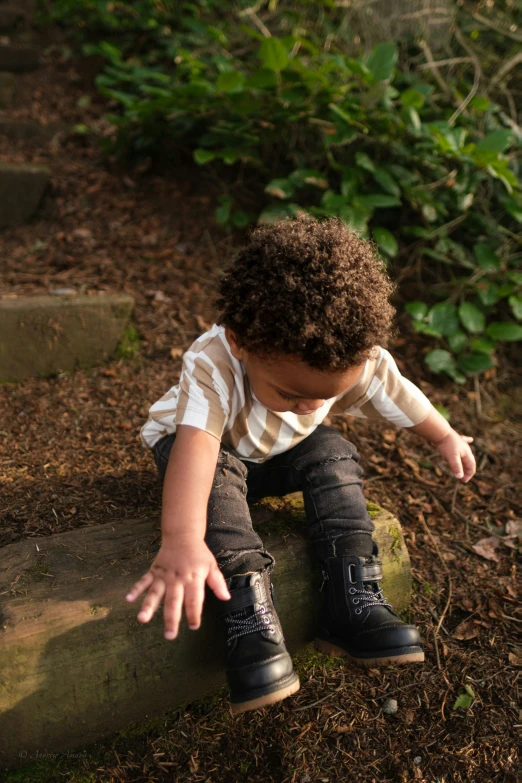 a small boy in black boots, crouches on a rock