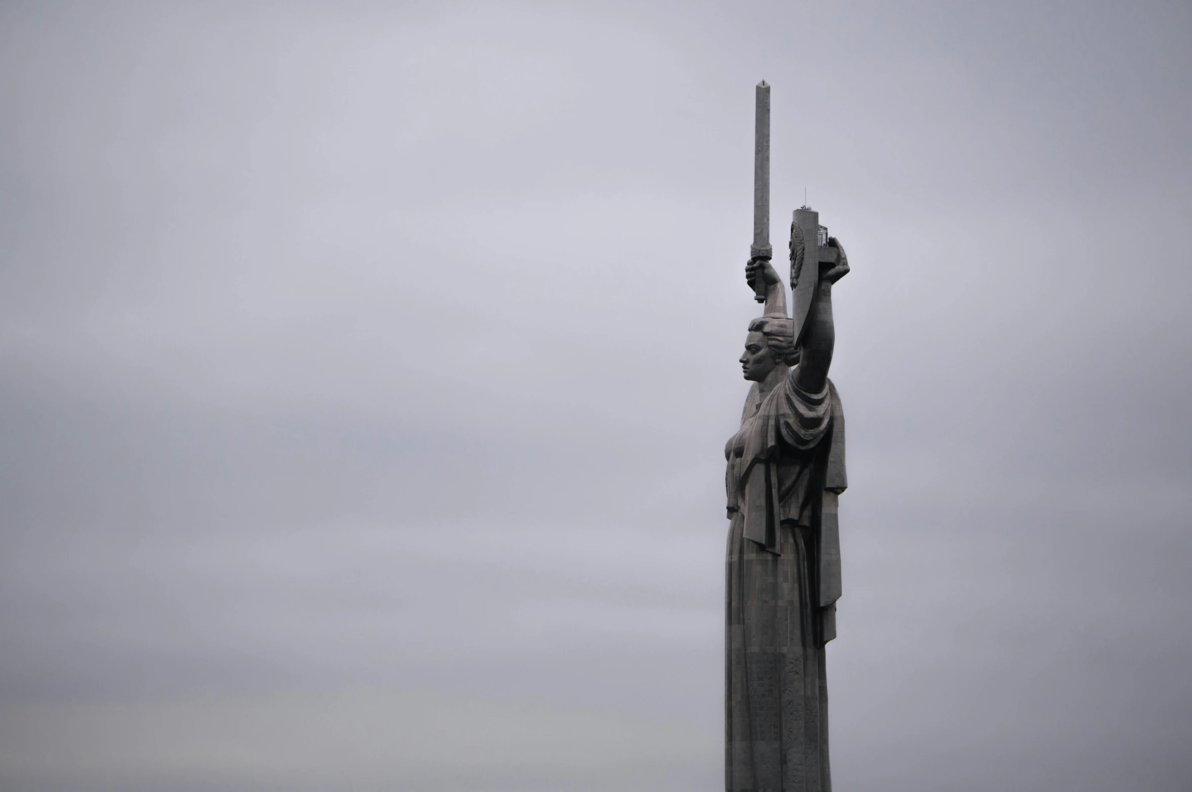 a statue with two swords in front of a cloudy sky