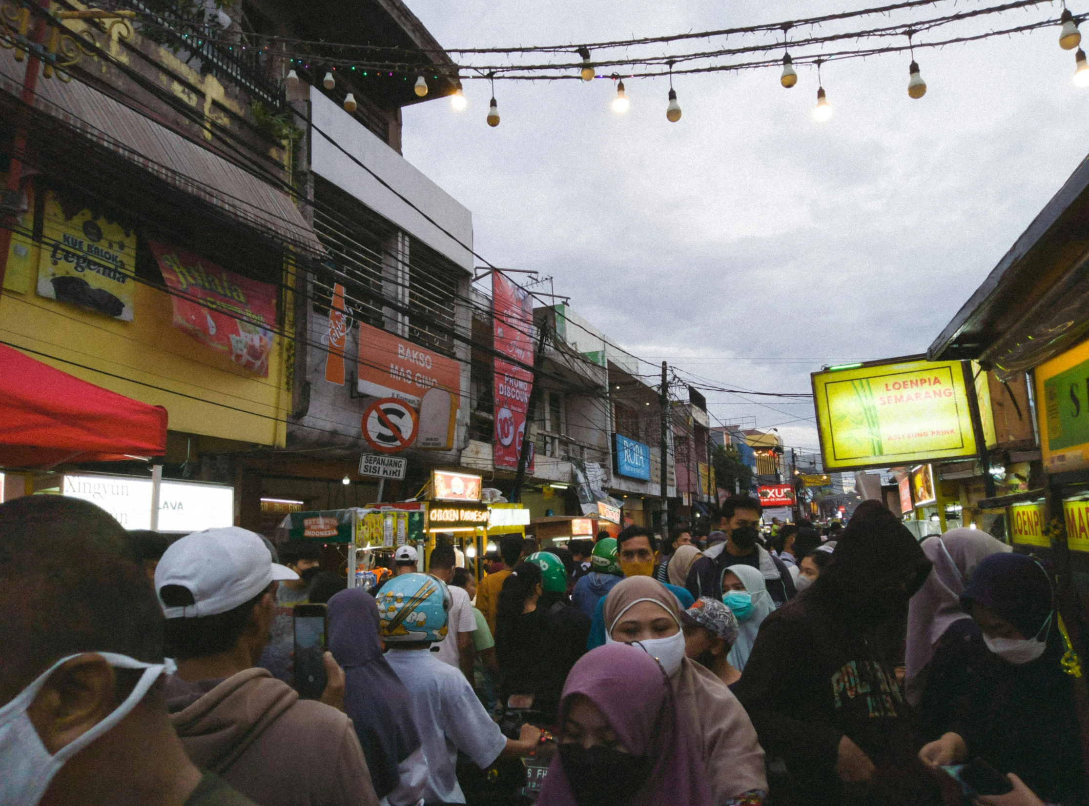 several people walking in the street with many lights hanging