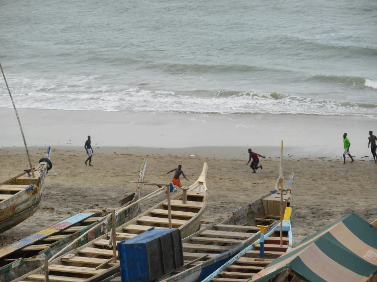 a group of people walking along the beach next to boats