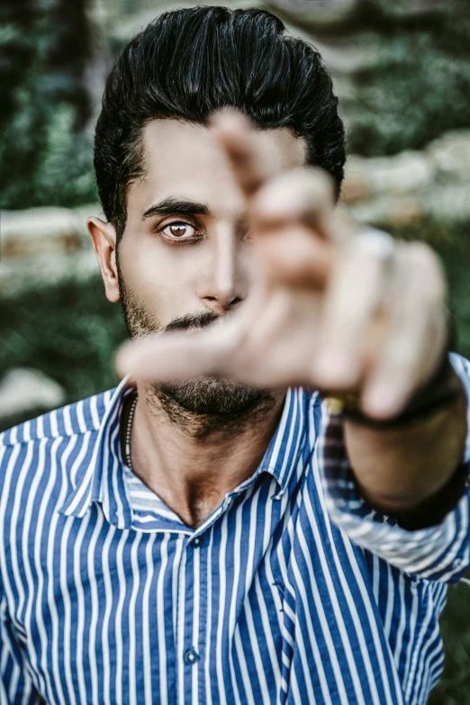 a man standing in a forest pointing at the camera with one hand