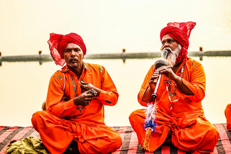 two men sit down, wearing bright orange outfits