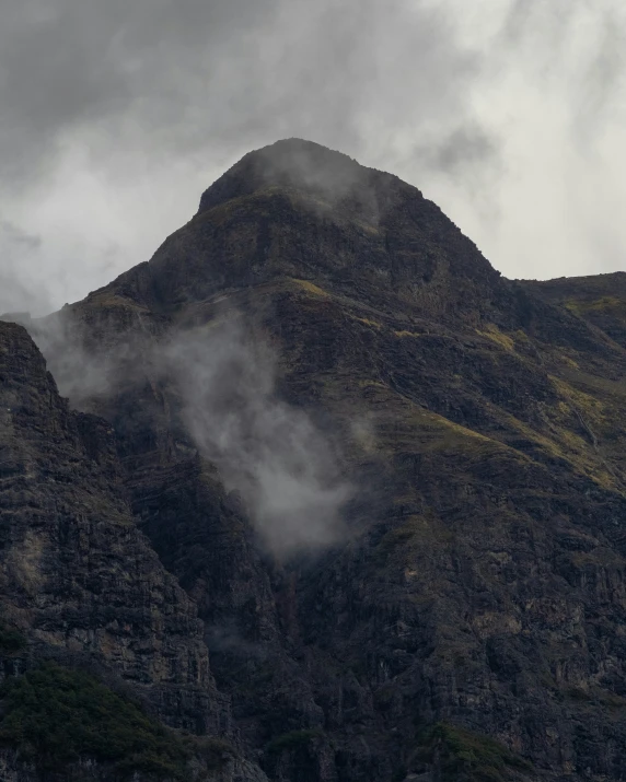 the top of a mountain with low clouds coming out of it