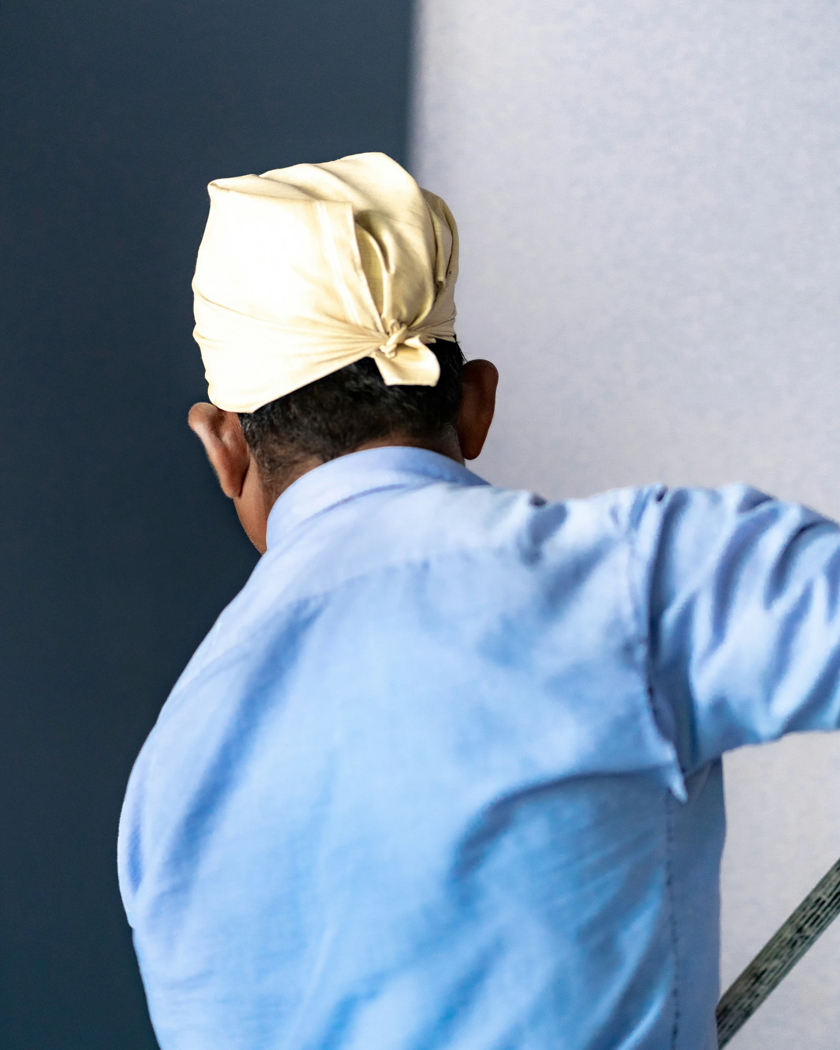 an older man wearing a yellow turban leaning on the wall