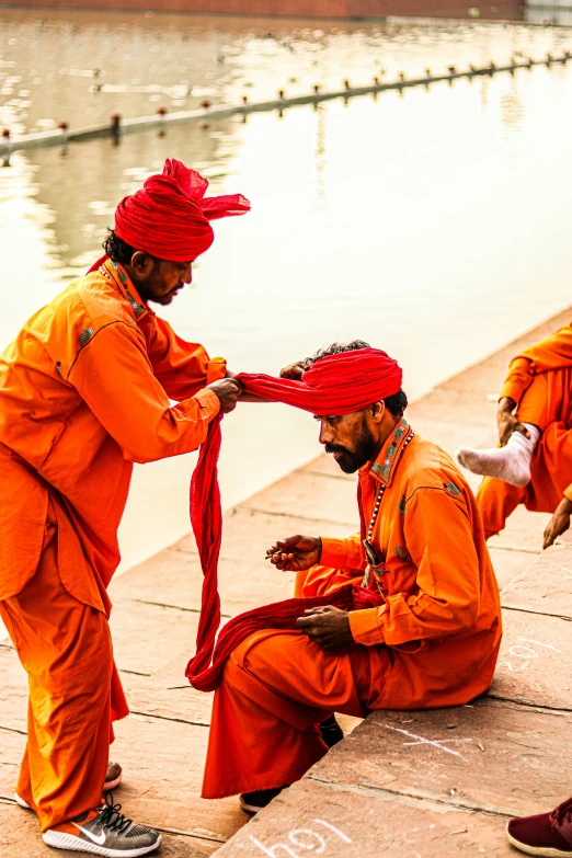 three men with orange outfits sit on the dock