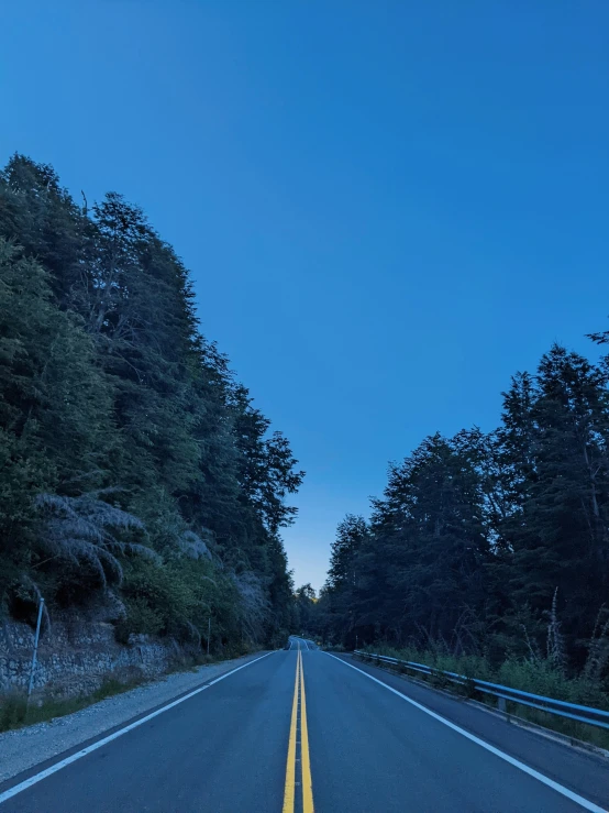 a long straight street is at the end of two lanes and has bright yellow painted edges