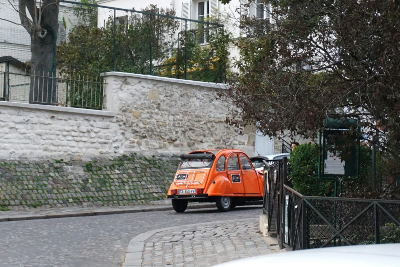 a small orange car sits on a cobblestone road