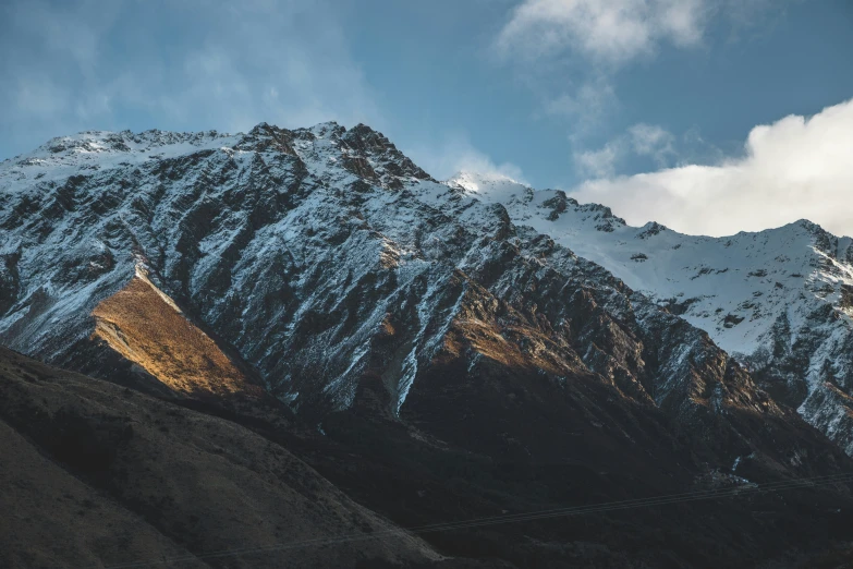 a snowy mountain range beneath a blue sky with clouds