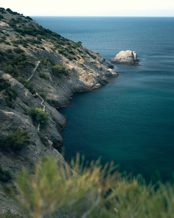 a cliff that leads into the ocean surrounded by hills and blue water