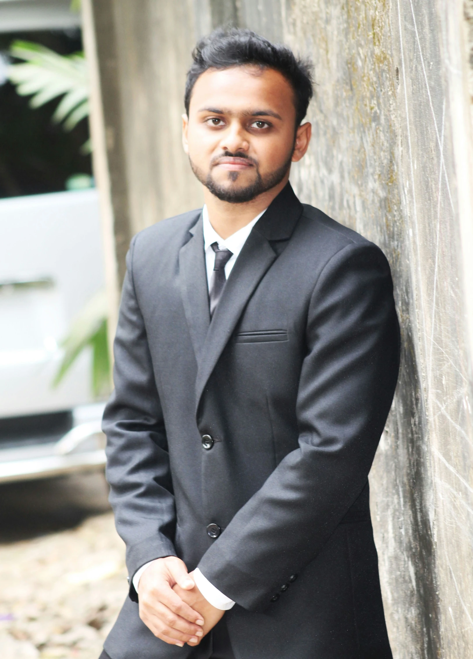 a man in a suit leaning against a concrete wall