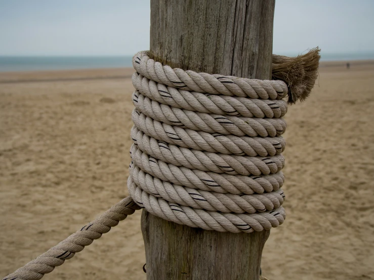 a rope wrapped around a wooden post in front of the beach