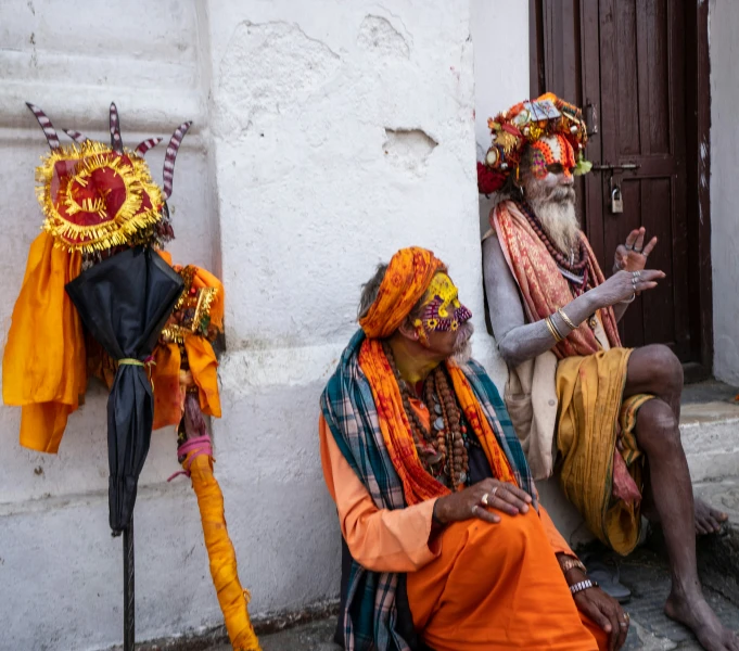 two indian men dressed in different colors sit near a wall