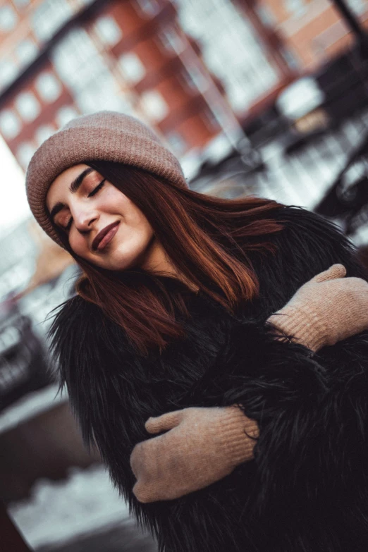 a girl standing outdoors with her arms crossed wearing a hat and fur coat