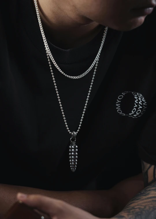 tattooed person in black shirt and white necklace sitting in front of his hand