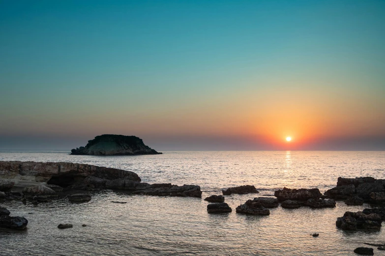 sunset over a large body of water with rocks and a rock formation in the middle