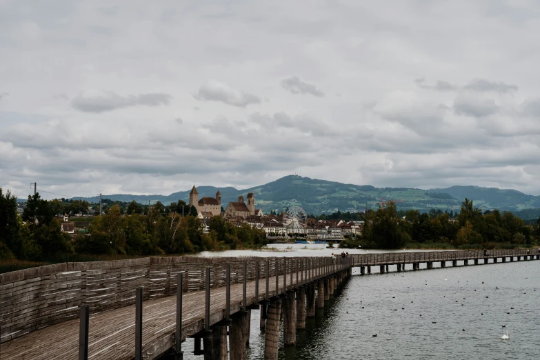 a wooden bridge spanning the width of a river with buildings behind it