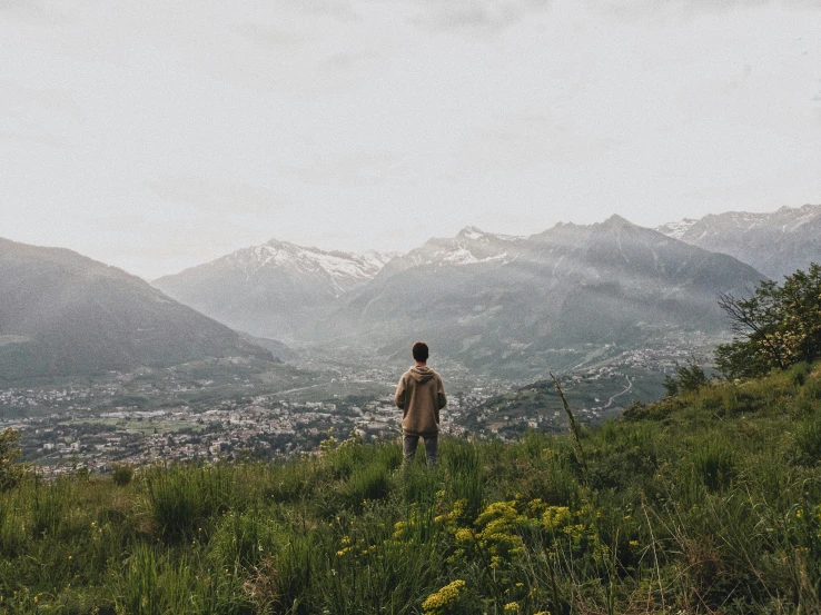 man standing alone on top of mountain overlooking city below