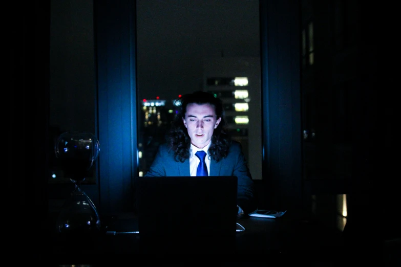 a dark po with a man in suit and tie on a laptop computer