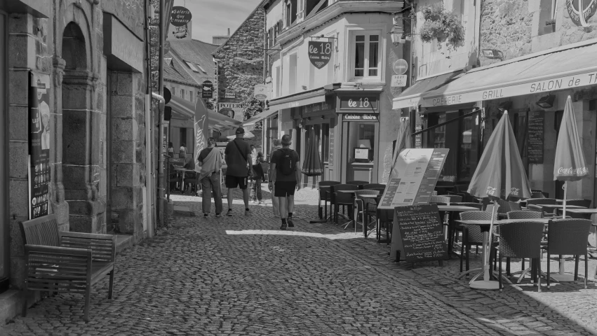 people walking in a cobblestone street with outdoor tables and chairs