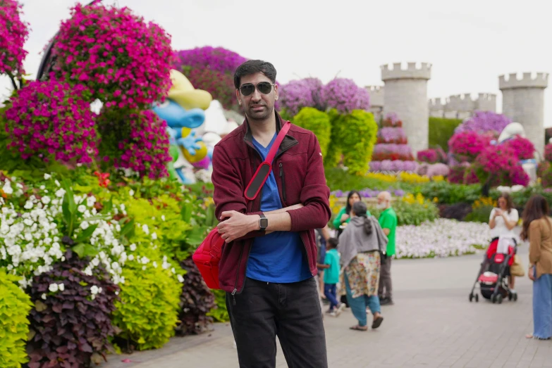 a man stands on a brick walkway with various colorful flowers