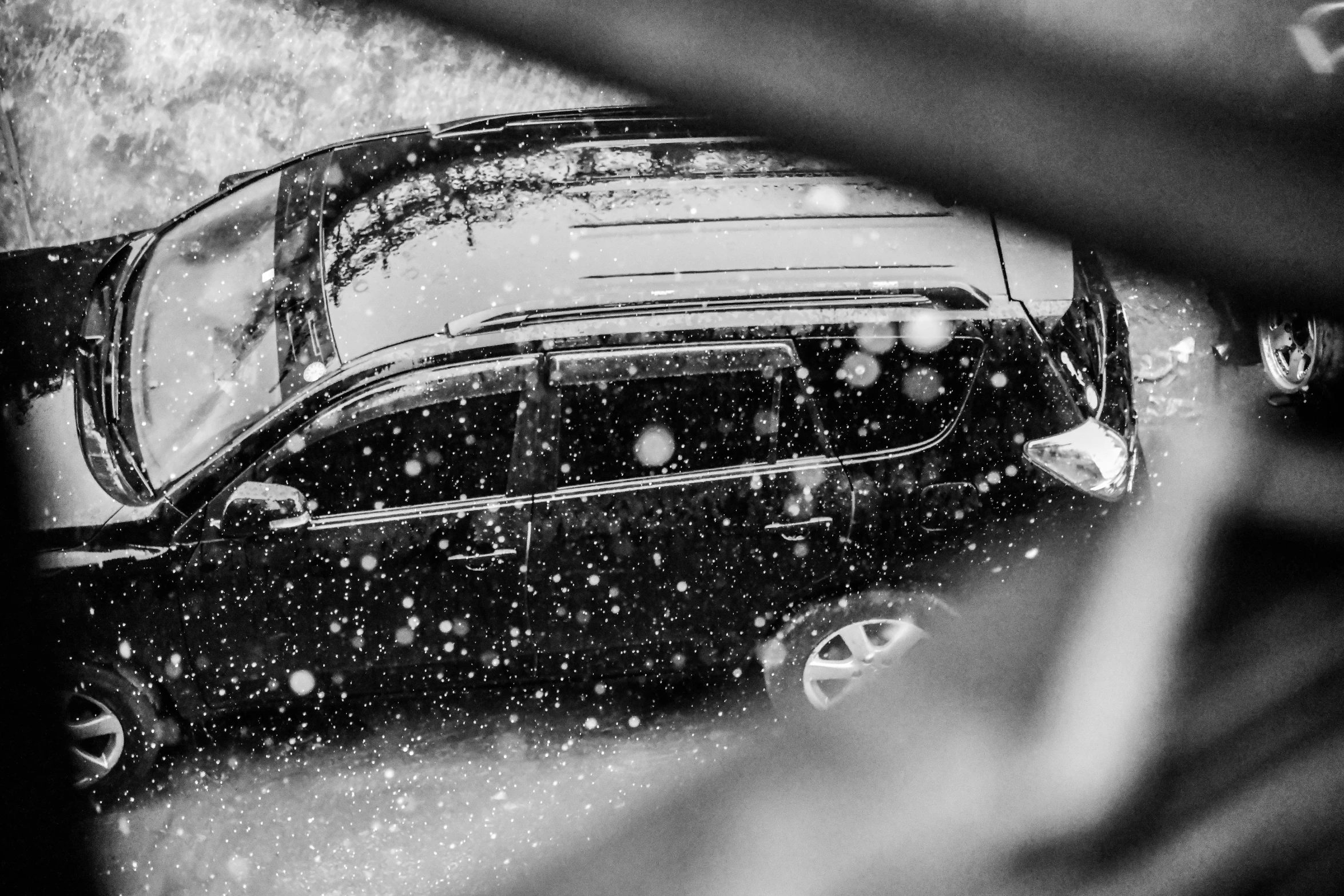 a rain - soaked, black car parked in a parking lot