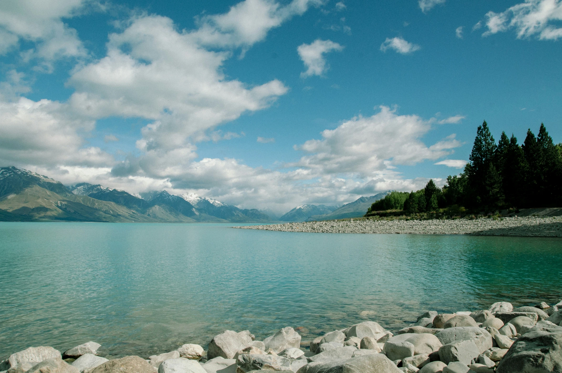 large rocks in the foreground of an empty lake with mountains in the background