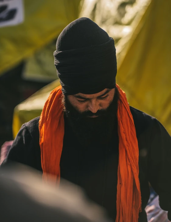 man in black hat and orange scarf standing next to tents