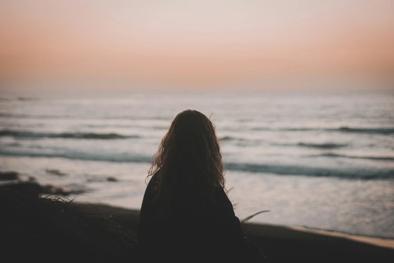 a woman is sitting in front of the ocean and looking at the waves