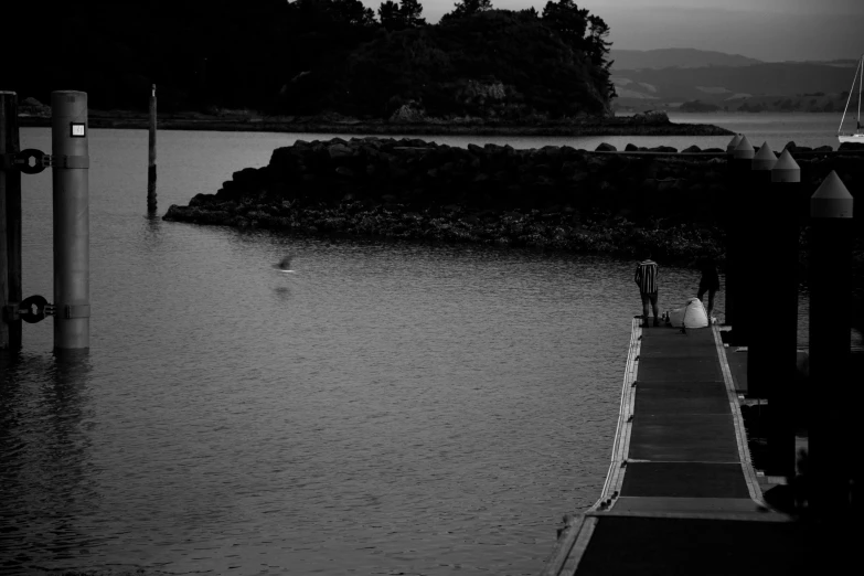 people on a pier looking out at the ocean in black and white