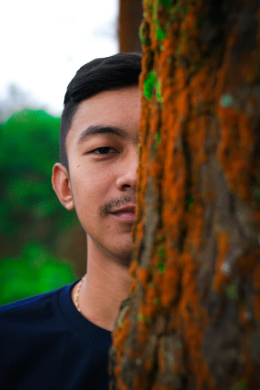 a young man standing next to a tree with green moss