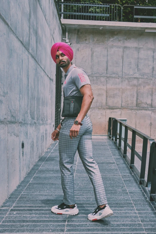 a man in a turban and grey pants poses on the sidewalk