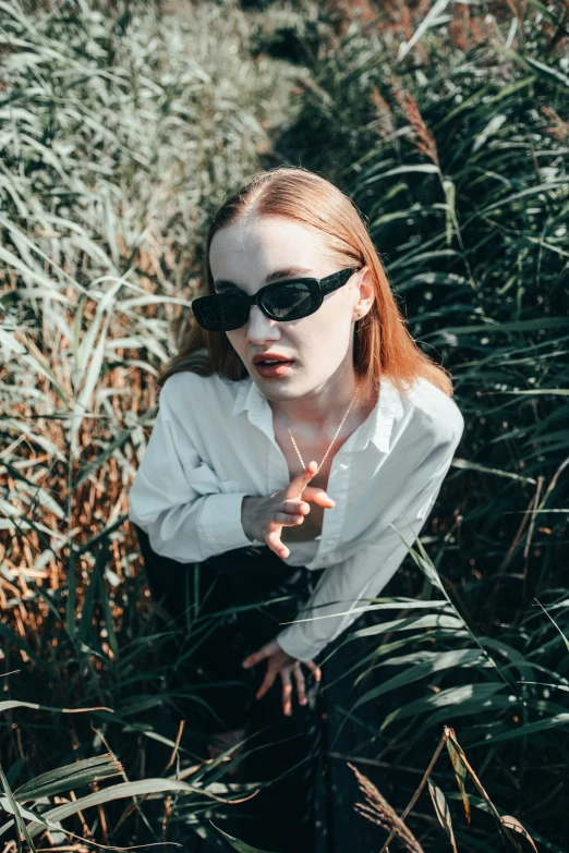 a girl is wearing sun glasses sitting in some tall grass