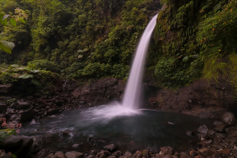 a tall waterfall next to rocks near a forest