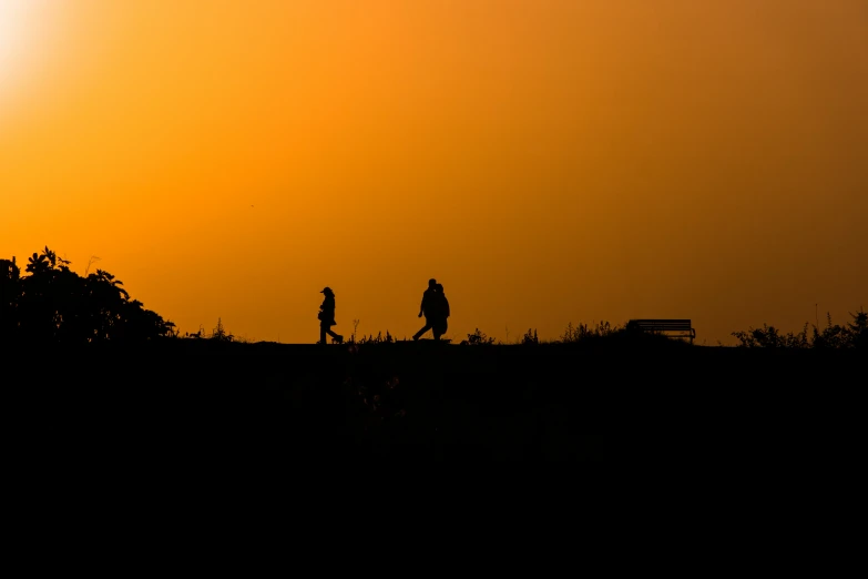 a silhouette of a man and woman are walking along the hill