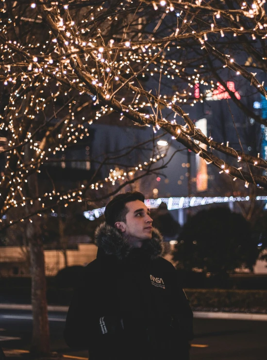 man in black jacket and a light up tree in the background