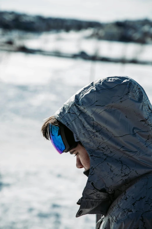 a man wearing a hood and sunglasses standing in the snow