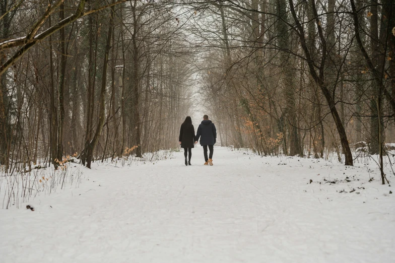two people are walking on the path in the woods