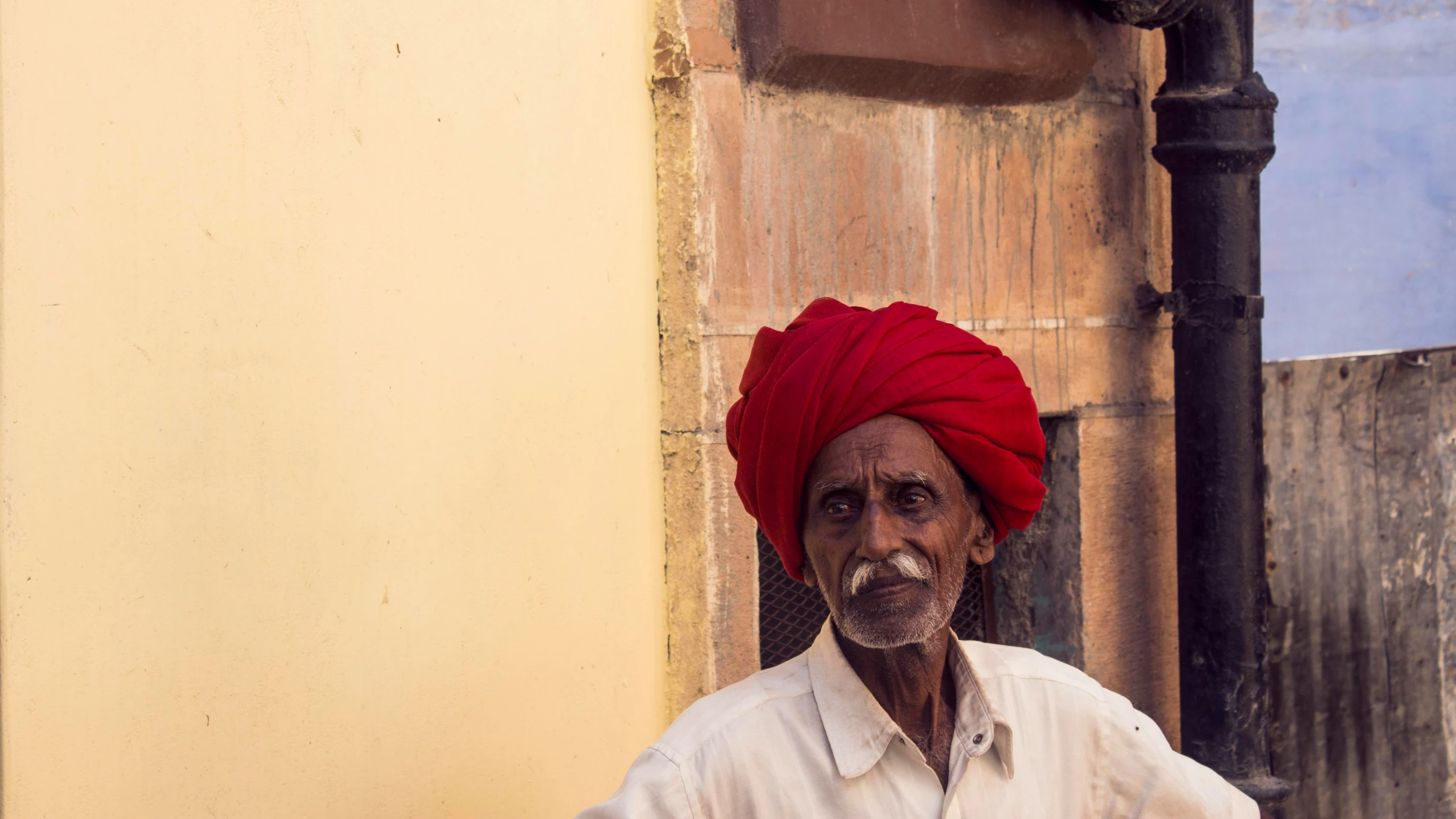 man in a red turban standing next to an old building