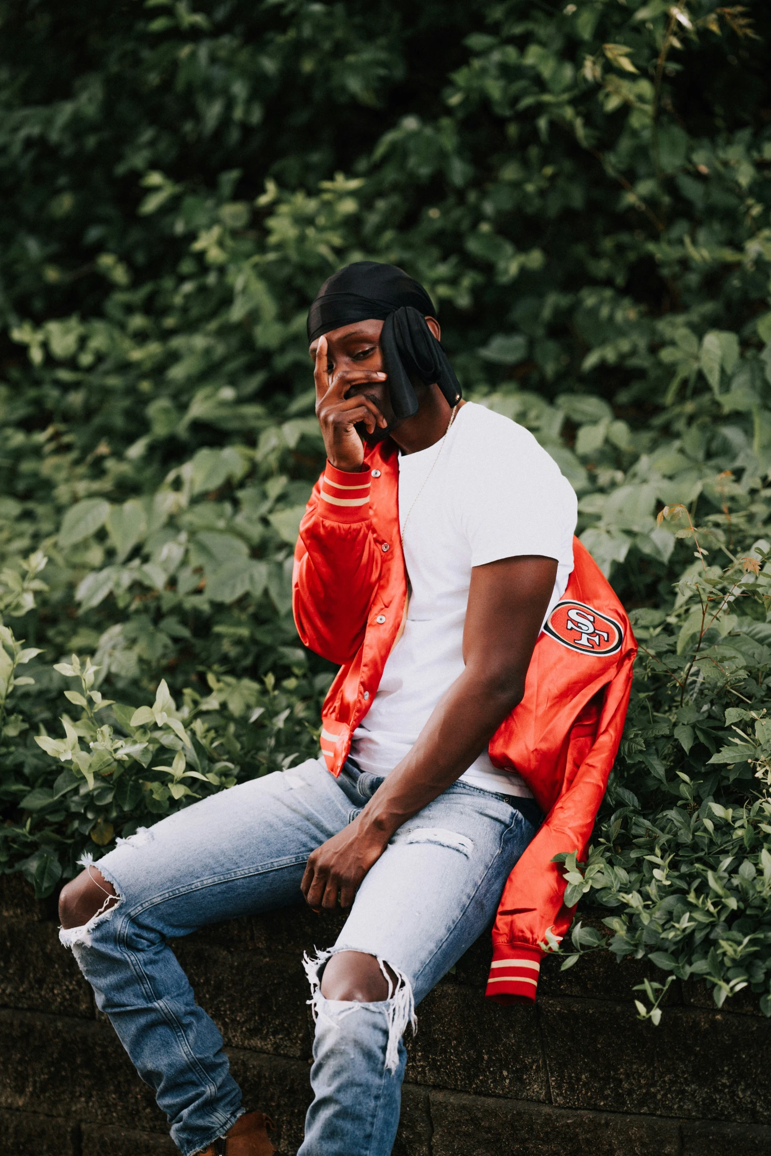 a person is smoking a cigarette and sitting on a cement slab with an orange jacket and jeans