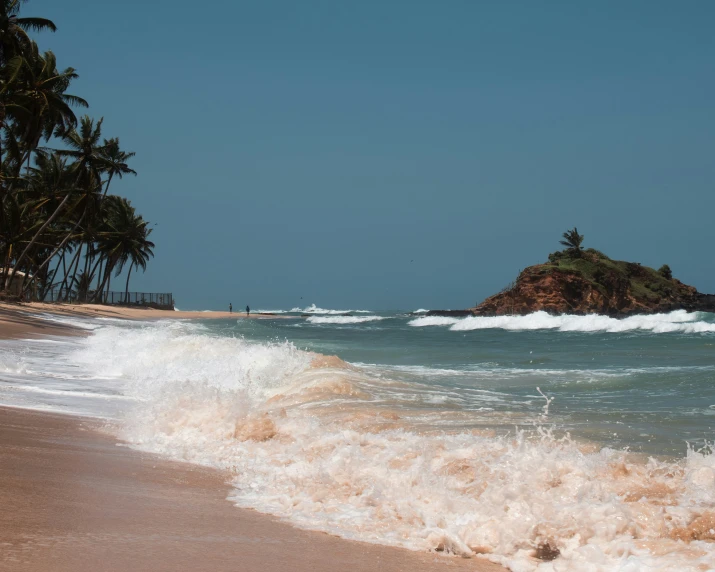 waves crashing on the sandy beach with an island in the background