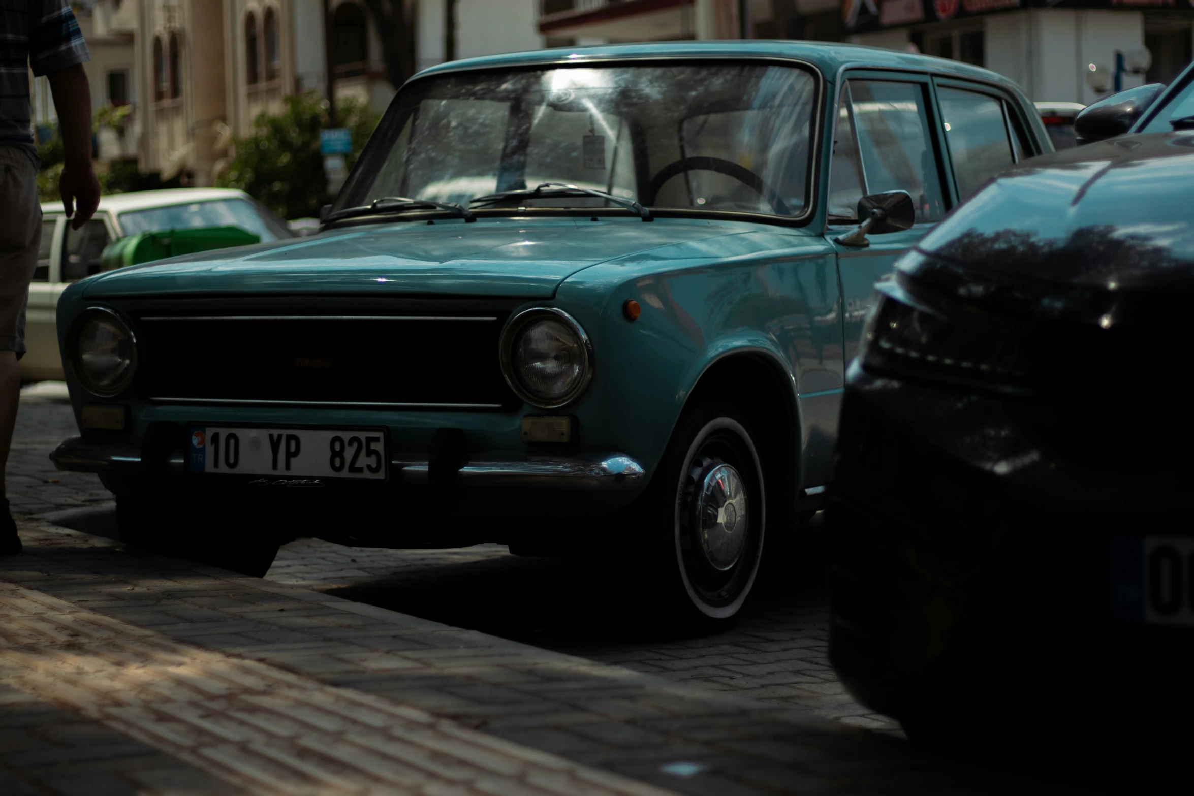 a small blue hatchback with its hood down on a street