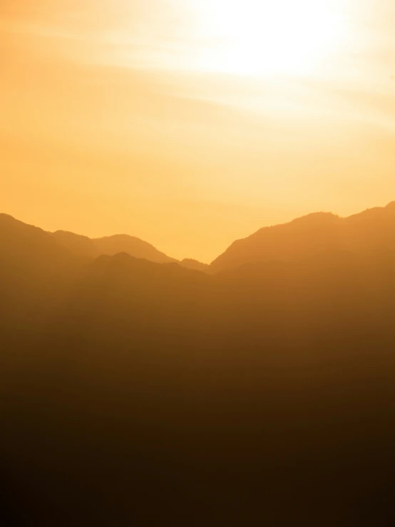 the sky above a couple of mountains as the sun is setting